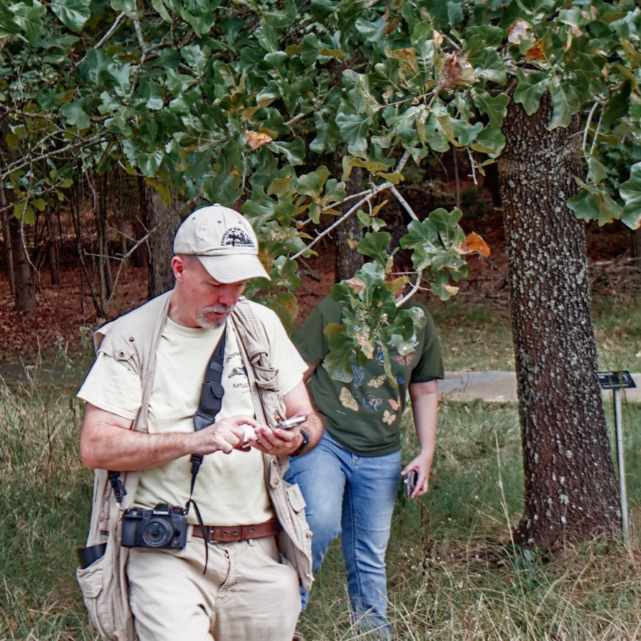 man dressed in khaki with camera, using a smart phone for citizen science