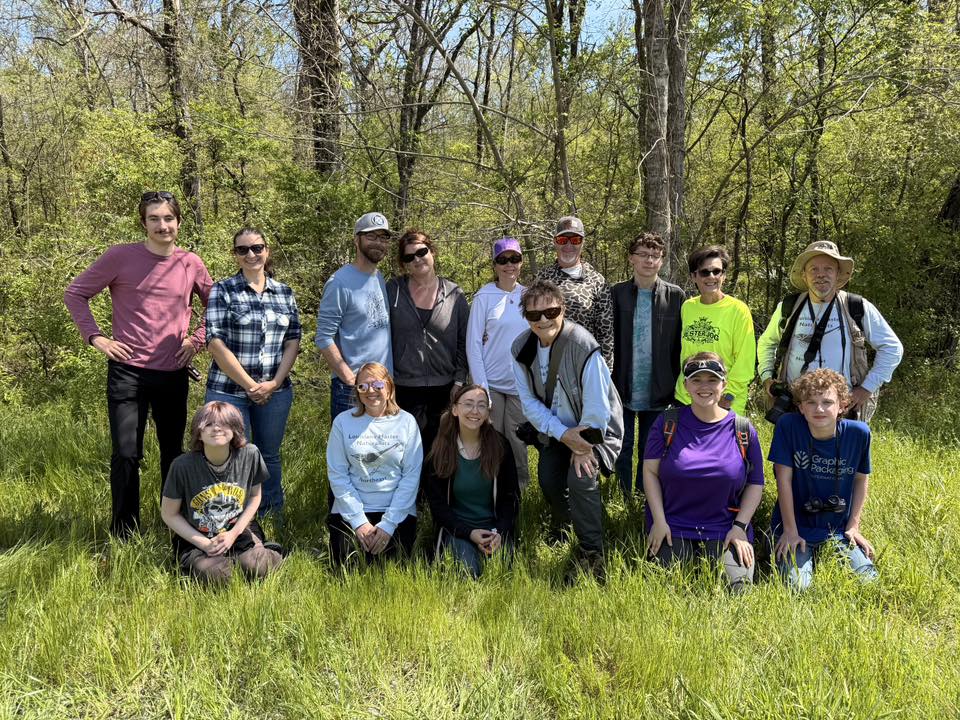 Naturalists in group photo on grass with forest behind them